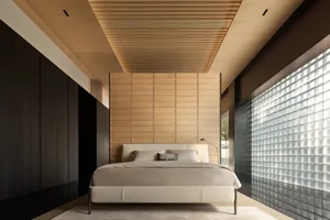 Modern minimalist bedroom with wooden paneled walls, white bed, and glass brick wall