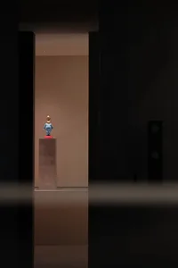 A small blue ceramic sculpture displayed on a pedestal in a museum setting.