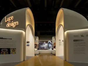 An interior view of an exhibition space featuring textured concrete archways and walls with a central screen displaying text