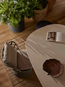 A modern setting featuring a sleek, circular concrete table with a small book and a decorative shell, surrounded by woven arm