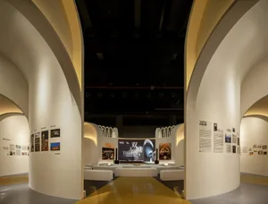 Modern exhibition space with gold accents, featuring a curved wall with artwork and a central display area.