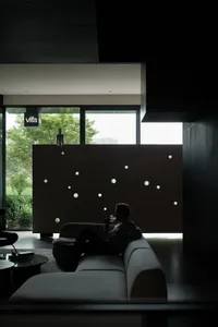 A modern interior space with concrete walls and a metal partition, featuring a person sitting on a sofa drinking from a glass