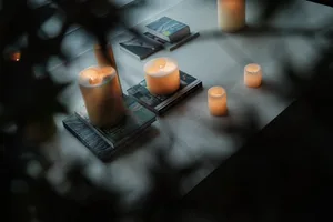 A cozy interior scene featuring candles on a table surrounded by books and greenery.