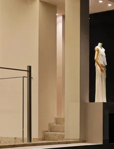 A mannequin dressed in a white ruffled dress, presented on a wooden form as part of a fashion exhibition display.