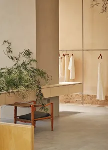 A minimalist retail store interior with clean lines, beige and cream tones, and a few hanging garments.