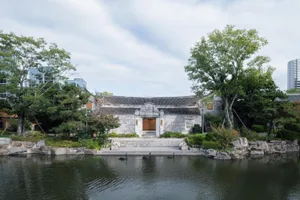 A traditional Chinese architectural building surrounded by a stone wall, with trees and black swans in the lake in front of i