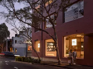 Modern building with exposed brick exterior during twilight hours with pedestrians walking by.