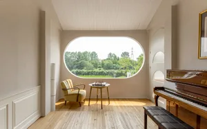 A minimalist living room featuring a yellow armchair, a small round table with a chessboard, and a piano bench.