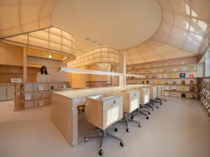A modern library with minimalist design, featuring wooden desks, fabric-covered shelves, and glass partitions.
