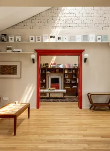 A modern living room with wooden floors and furniture, showcasing a white bench, a coffee table, and a bookshelf filled with 