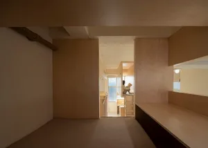 A modern minimalist living room featuring a wooden floor and walls, with a person sitting on a platform reading a book.