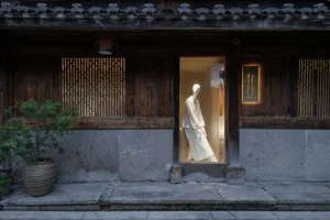 櫥窗展示中，一尊穿著傳統白色服裝的人體模型，背景為木質店面與格子窗。