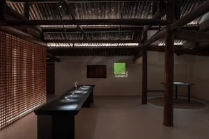 Ceramic cups and saucers displayed on a long wooden table with light filtering through a grid wall in a modern tea room setti