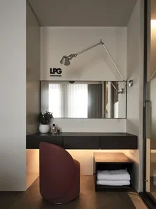 A modern minimalist bedroom with a red chair, a floating desk, a large mirror, and a towel on a shelf.