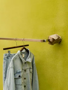 Clothing display with denim jacket and jeans hanging on metal hangers attached to a yellow textured wall.