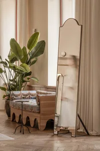 A modern living room featuring wooden furniture and glass elements, with a plant and a mirror in the background.