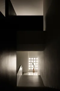 A minimalist interior space with a concrete wall and a person standing in front of a lighted wall featuring circular patterns