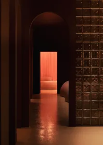 A dark, minimalist hotel room featuring metallic surfaces and a lounge area.