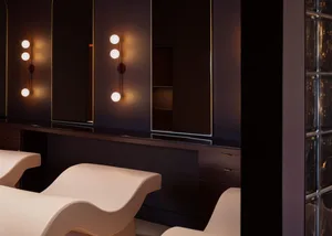 A modern beauty salon features a row of illuminated mirrors, glass partitions, and sleek seating areas.