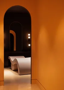 Modern interior space with an arched doorway, orange walls, and a white curved bench.