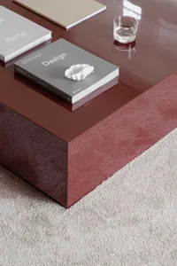 Modern coffee table with glass top and red base on a gray carpet