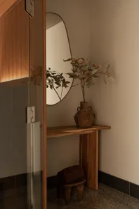 An elegantly decorated minimalist entrance hall features a carved wooden bench and a ceramic vase with greenery.
