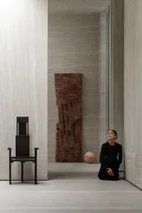 Minimalist interior space featuring concrete walls and floor, with a black rectangular chair and a large orange marble sphere