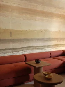 A modern living room featuring a coral-colored sofa with a textured, abstract mural backdrop.