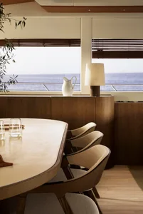 A modern dining room with a wooden table, beige upholstered chairs, a white vase, and a lamp.