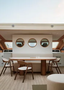 A modern yacht lounge featuring a sleek, white table with wooden legs, surrounded by cushioned chairs with wooden frames.