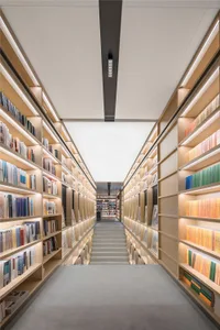 A modern, spacious library with tall bookshelves filled with books, illuminated by soft lighting from within the shelves.