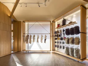 現代零售店內，白色的釘板牆上懸掛展示各式服裝，搭配多款背包與配件
