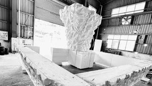 A modern sculpture crafted from cast stone with a textured, abstract design in an indoor workspace.