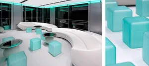 A modern commercial interior featuring white curved couches, blue cube stools, and glass tables with blue LED lighting.