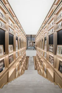 A modern library with wooden shelves filled with books, viewed from the staircase leading upwards.