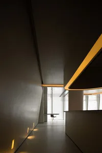 Minimalist modern office space with concrete walls, accent lighting, and a window providing natural light.