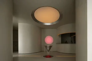 A minimalist interior space with concrete walls, featuring a large circular light fixture and a transparent cylindrical struc