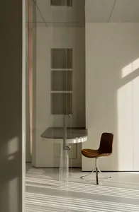 Modern minimalist office space with glass desk and chair, featuring sleek lines and natural light.
