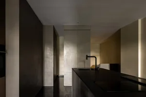 A minimalist residential kitchen with concrete countertops and walls, featuring high-contrast lighting and sleek, modern appl