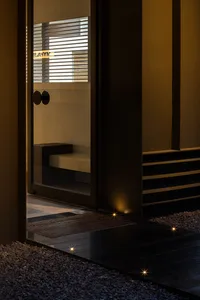 A modern entrance featuring a glass door, concrete steps, and gravel pathway illuminated by warm lights.