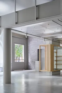 Modern indoor space with concrete walls and floor, large open area, large natural light openings, and minimalist furniture de
