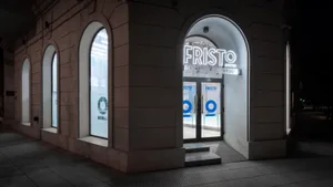 Night view of a storefront with concrete walls and a large arched entrance, illuminated by neon signage.