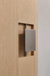 Minimalist metallic door latch embedded in a wooden door.