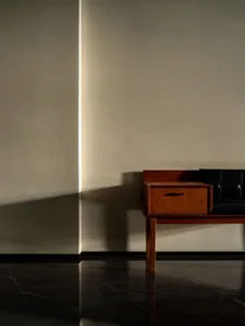A minimalist interior with a wooden table and black leather seating against a plain wall and marble floor.