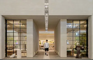 A walkway covered in grey concrete surrounded by glass doors and columns.