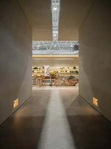 A minimalist commercial space featuring a concrete floor and walls, industrial-style lighting, and a central piece of furnitu
