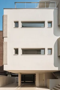 A modern building with a concrete exterior featuring large windows and a rooftop balcony.