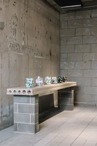 Modern industrial concrete counter with jars containing various items against a raw concrete wall background.