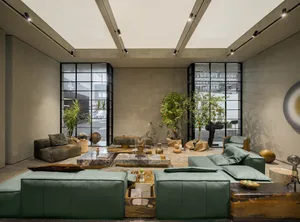 A modern, minimalist living room with concrete walls, furniture, and lighting, featuring green sofas and decorative plants.