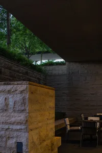 Modern outdoor seating area with stone walls and greenery in the background.